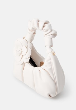 Mała miękka biała torebka z marszczonym uchwytem i dużym kwiatowym zdobieniem z przodu, otwarta góra z magnetycznym zapięciem.