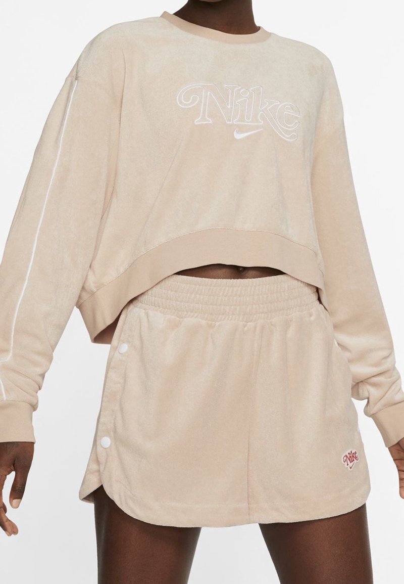 Beige, pl plush sweatshirt med Nike-logotyp, cropped design och långa ärmar. Matchad med högmidjade shorts med knappar.