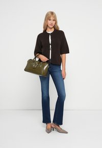 Brun kortärmad cardigan, vit topp, blå utställda jeans, grå högklackade skor och en olivgrön handväska med dekorativa metalldetaljer.