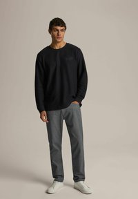 Granatowy sweter z okrągłym dekoltem, szare strukturalne spodnie oraz białe sneakersy, z delikatnym logo na piersi.