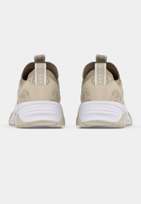 Chaussures de sport beiges avec une tige en tricot texturé, une semelle en caoutchouc blanche et une languette à l'arrière ornée de "GUESS" en bleu clair.