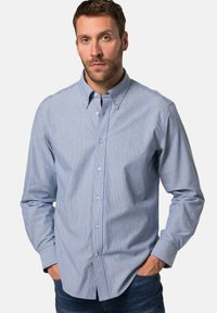 Camicia a righe blu e bianche con colletto, maniche lunghe e bottoni visibili, realizzata in un tessuto liscio. Indossata con jeans.