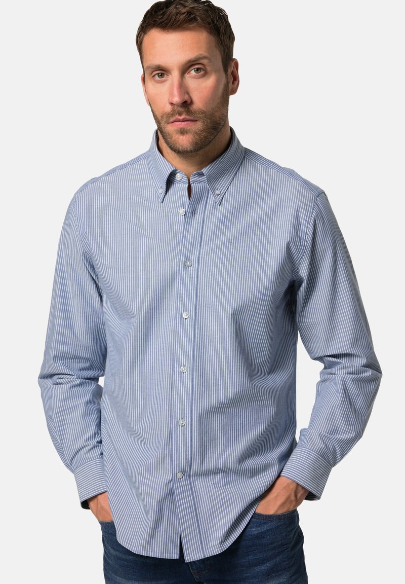 Camicia a righe blu e bianche con colletto, maniche lunghe e bottoni visibili, realizzata in un tessuto liscio. Indossata con jeans.