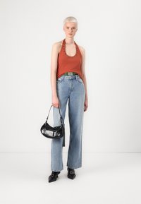Top halter en rustique avec des détails en œillets, jeans taille large bleu clair, sac à main noir et chaussures noires à bouts pointus. Textures lisses et design décontracté.