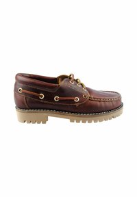 Zapato de barco de cuero marrón con punta redondeada, ojales dorados y suela de goma naranja que presenta un patrón de textura en la banda de rodadura. Se aprecian detalles de costura.