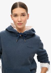 Sudadera azul marino hecha de una suave mezcla de algodón, cuenta con capucha con cordón, bolsillo tipo canguro y logo bordado en el pecho.