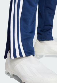 Marinefarbene Sporthosen mit drei weißen Streifen an den Seiten, kombiniert mit weißen Schuhen, die über strukturierte Muster und ein elegantes Design verfügen.