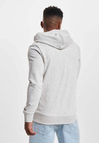 Lys grå hettegenser med en romslig hette, ribbede mansjetter og kant, laget av mykt materiale. Har et minimalistisk design uten grafikk.
