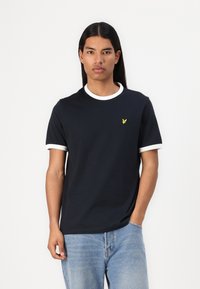 T-shirt bleu marine foncé en coton, avec des poignets de manches courtes blancs et un col rond. Un petit logo jaune est présent sur la poitrine.