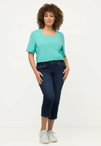 Vihreä nelikulmainen paita lyhyellä hihalla, yhdistetty tummansiniin lyhythihaisiin farkkuihin ja valkoisiin lenkkareihin. Liukas kangas ja istuva muotoilu.