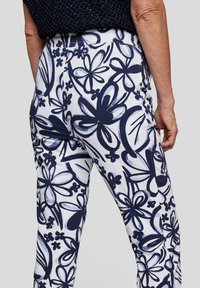 White pants with a navy floral pattern, featuring large butterfly shapes and flowers. Smooth fabric, high waistband, fitted design.