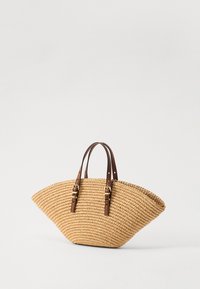 Stråhandtaske med en bred, buet form, der har to brune læderhåndtag og spænde detaljer. Teksturert vævet finish.