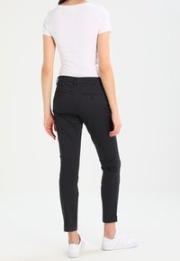 Czarne spodnie slim fit wykonane z mieszanki bawełny, o średnim stanie, z tylnymi kieszeniami i wykończeniem do kostek, w połączeniu z białymi sneakersami.