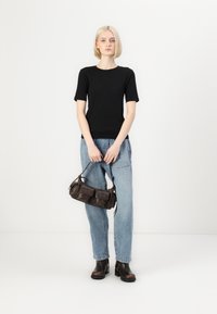 Černý krátký rukáv top doplněný světle modrými džíny a černými kotníkovými botami. K outfitu ladí tmavě hnědá kabelka se dvěma předními kapsami.