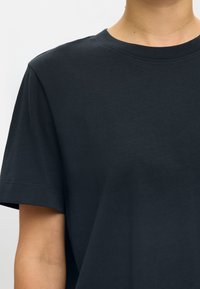 Tamsiai mėlynas medvilninis marškinėlis su apvalia iškirpte, trumpomis rankovėmis ir lygiu audiniu. Turi paprastą dizainą be raštų ar papuošimų.