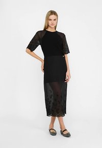 Schwarzes Kleid mit tailliertem Oberteil, transparenten, floralen kurzen Ärmeln und einem mittellangen, mehrlagigen Rock mit bestickten Details am Saum.