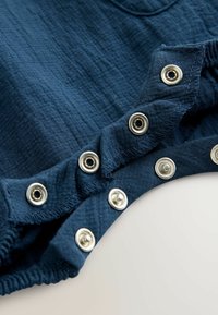 Navyblauwe katoenen stof met een gekreukt textuur heeft metalen drukkers langs de rand, wat de duurzaamheid en het gebruiksgemak verhoogt.