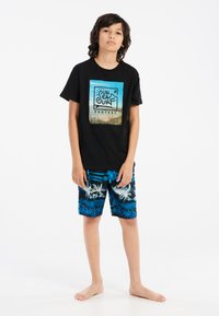 Camiseta de algodón negra con un gráfico de playa, combinada con bañadores cortos azul y negro con un diseño de palmeras.