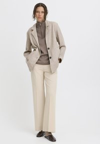 Beige wolmix blazer met gesneden revers, twee knopen en zijzakken, gecombineerd met een lichtbruine trui met hoge hals en crèmekleurige culottebroeken.