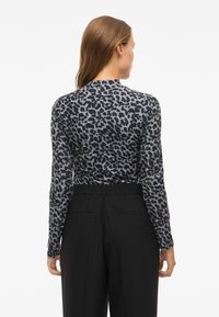 Long-sleeve top in grey with black leopard print. Lightweight fabric with a slim fit, paired with high-waisted black trousers.