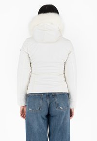 Chaqueta acolchada blanca con capucha de piel sintética, textura acolchada y costuras contrastantes. Combinada con unos vaqueros de mezclilla azul de talle alto.