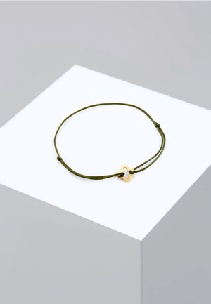 Grøn snorarmbånd med en charm i guldtonet metal i kløverform. Charmet har glatte kanter og en poleret overflade.