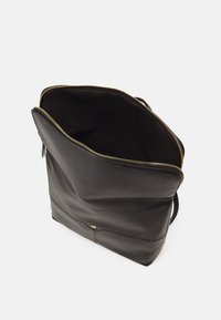 Černý kožený batoh se zlatým zipem, částečně otevřený, ukazující tmavý interiér na bílém pozadí.