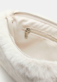 Bijela lažna krzna torbica s glatkom unutarnjom podstavom i detaljima od srebrnog zatvarača. Sadrži dodatni džep na zip za male predmete.