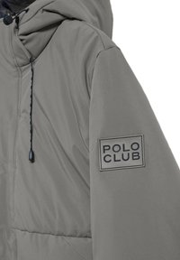 Chaqueta acolchada gris con capucha, que presenta una tela texturizada, bolsillo frontal y un logo rectangular "POLO CLUB" en la manga.