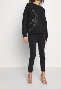 Sweat-shirt noir surdimensionné, jean noir déchiré et talons blocs beiges à brides. Le sac bandoulière comporte des fermetures éclair et un détail chaîne.