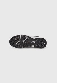 Semelle de sneaker noir et blanc avec un grip texturé et un logo "S" stylisé blanc centré au bas.