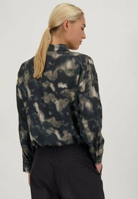 Langarmshirt in donkere tinten met een wolkenachtig patroon, voorzien van een kraag en knoopsluiten, gemaakt van luchtige stof.