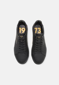 Svarta lädersneakers med rund tå, platta snören och präglad guldlogotyp. Utrustad med guldtryck "1973" på innersulorna, texturerad yta och elegant design.