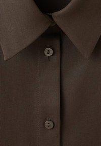 Close-up van een bruine boord van een overhemd met twee zichtbare knopen, vastgemaakt langs de voorste knoopsluiting.