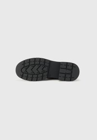 Semelle en caoutchouc noir avec un motif texturé en zigzag pour l'adhérence, dotée d'un design plat et épuré et d'une finition mate uniforme.