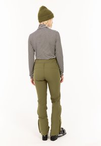 Gestreepte lange mouwen top en olijfgroene broek. De broek heeft een aansluitend ontwerp en zijritsen. Zwarte laarzen met merknaam op de zool.