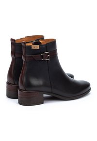 Botas de tobillo de cuero negro con una tira de cuero marrón y un acento de hebilla plateada. Punta redonda y tacón bajo apilado. Forro interior suave.