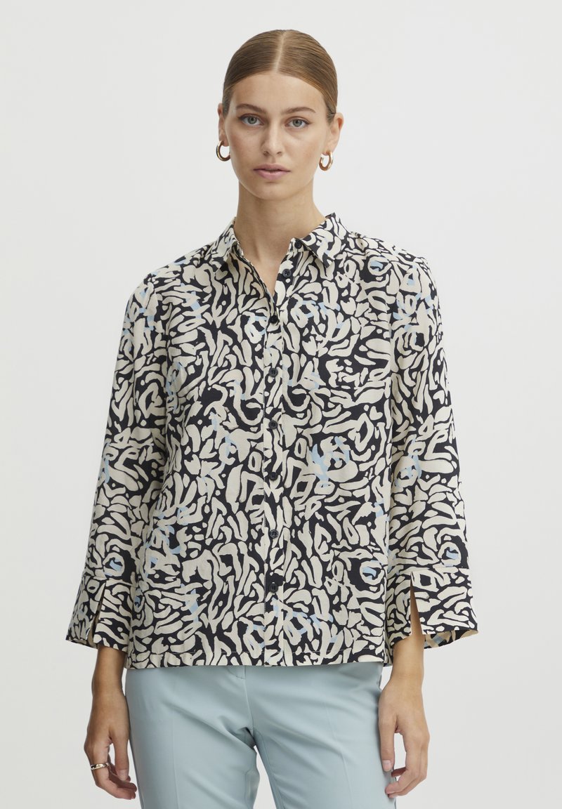 Knoop-up shirt van lichte stof, met een zwart en crème abstract patroon met blauwe accenten. Lange mouwen met zijsplitten aan de zoom.