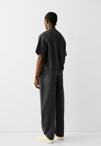 Tmavě šedý outfit skládající se z pulovru s krátkým rukávem a kalhot s širokými nohavicemi, obojí s měkkou texturou a minimalistickým designem.