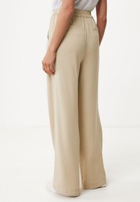 Pantalons large beige clair en tissu lisse, dotés d'une taille élastique, de poches latérales et d'une coupe décontractée.