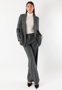 Completo in misto lana grigio con blazer doppiopetto e pantaloni a gamba larga. Include un dolcevita aderente e eleganti décolleté nere con punta affusolata.