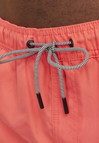 Bañador de coral con cinturilla elástica, que presenta un cordón en zigzag negro y blanco con puntas de plástico y costuras detalladas.