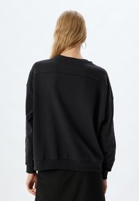 Felpa nera oversize realizzata in morbido cotone, con scollatura a girocollo, spalle scese e polsini e orlo a costine.