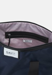 Navyfarbener Stoffbeutel mit schwarzem Reißverschluss, pinkem Innenfutter und kleiner Innentasche. Markenlabel an der Außenseite sichtbar. Strapazierfähiges Design.