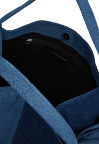 Ανοιχτή μπλε τσάντα από τζιν με μαύρη εσωτερική επένδυση, διαθέτει φόρμα με φερμουάρ και κλείσιμο με κουμπί.