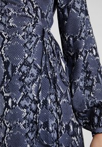 Navyblaues Wickelkleid mit Schlangenmuster, strukturiertem Stoff, langen Puffärmeln und einem Bindegürtel in der Taille.