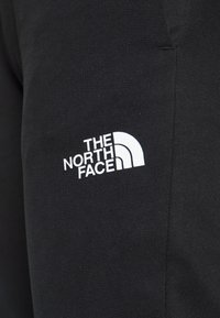 Sorte bomuldsjoggingbukser med et hvidt logo fra "THE NORTH FACE" i et buet design. Tekstureret stof, tætsiddende ved anklen.