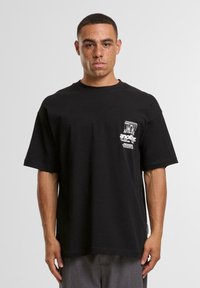 Tricou negru din bumbac cu mâneci scurte, guler rotund și un grafic imprimat pe pieptul stâng. Croială lejeră, casual, cu o textură netedă.