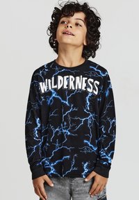 Maglietta nera a maniche lunghe con un motivo a fulmine blu e la parola "WILDERNESS" in lettere bianche in grassetto sulla parte anteriore.
