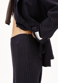 Marineblau gestreifter Anzug mit schmaler Passform. Verfügt über ein maßgeschneidertes Sakko und Hosen mit Reißverschluss, ergänzt durch kontrastierende Stoffakzente.